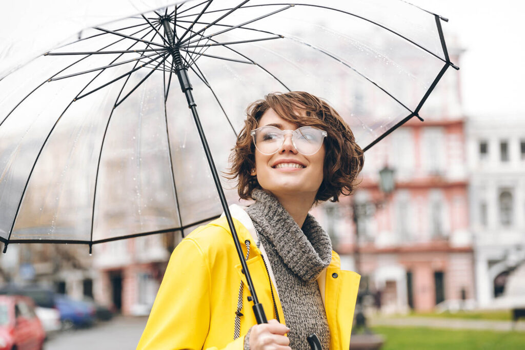 Woman in yellow rain jacket under a clean umbrella in rain