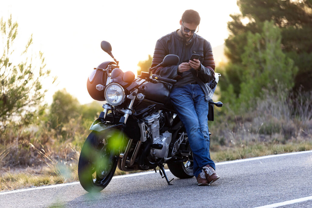 Man sitting on parked motorcycle reviewing motorcycle insurance quotes from Quaint Oak Insurance on phone