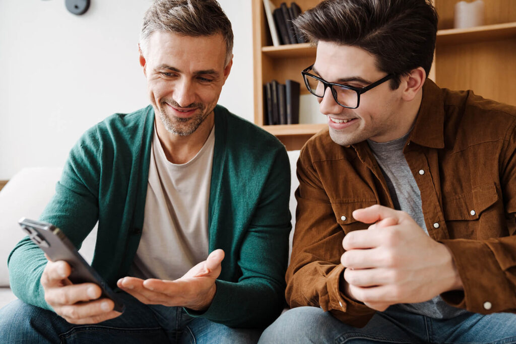 Two men smiling looking at insurance quotes on smartphone from Quaint Oak Insurance