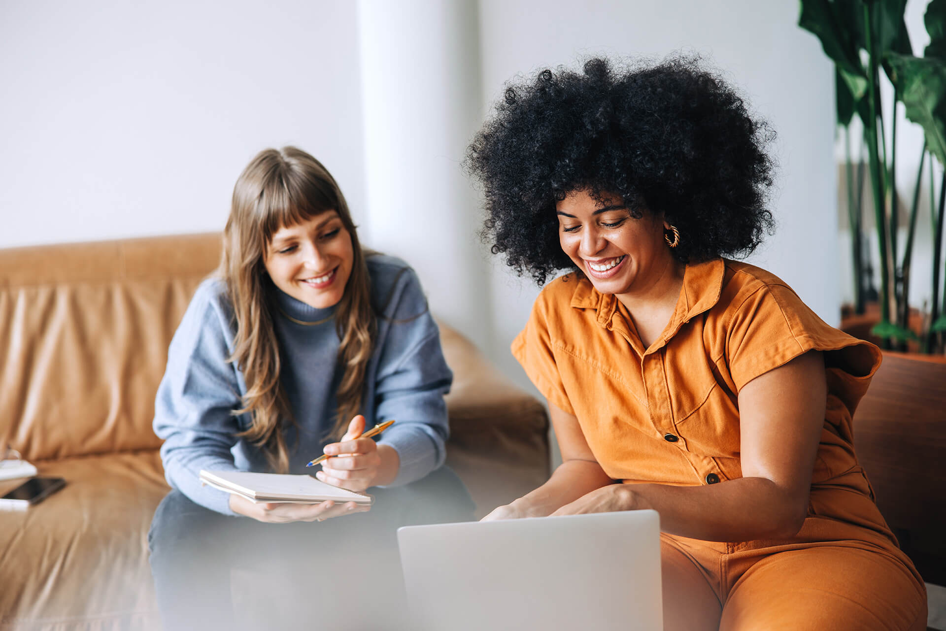 Two young woman smiling around a laptop on table