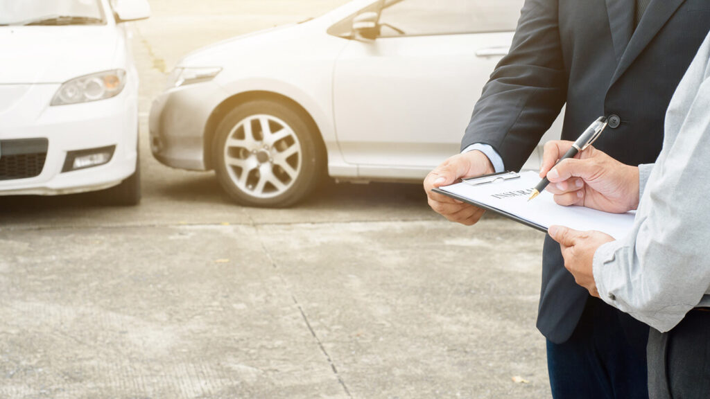 Two people signing auto insurance documents after automobile accident