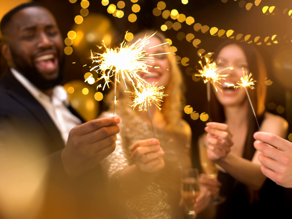 a group of friends celebrate the new year with sparklers after learning how to host a safe holiday party