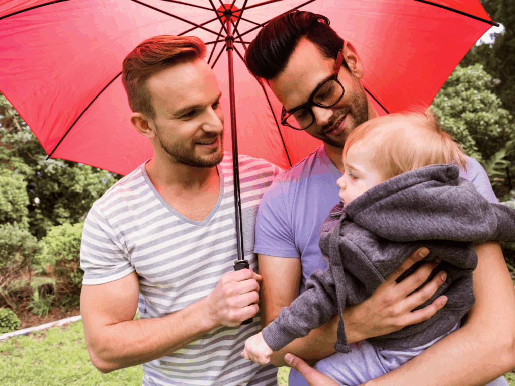 a couple holds their child under a red umbrella as they discuss is an umbrella policy worth having